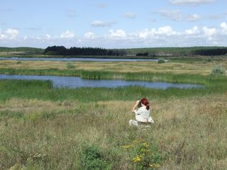 Eine Rangerin beim Monitoring mit einem Fernglas auf einer weiten Wiesenlandschaft mit kleinen Seen